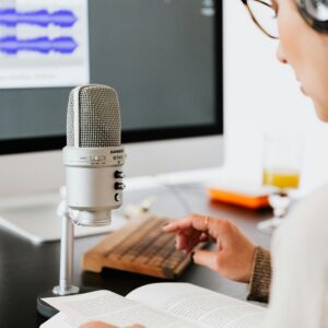 Person wearing headphones reading from a book with a microphone. Ideal for podcasts.